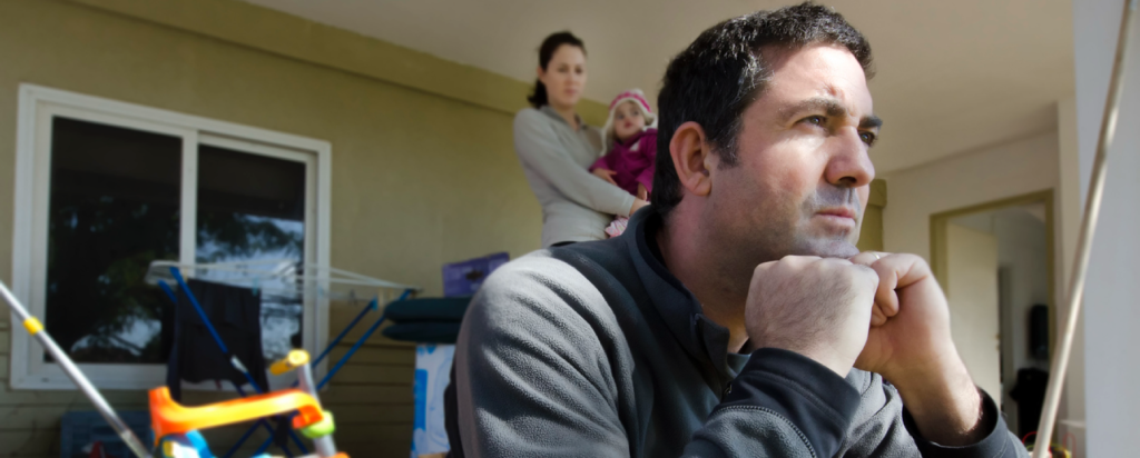 Man looking worried with wife holding baby in the background